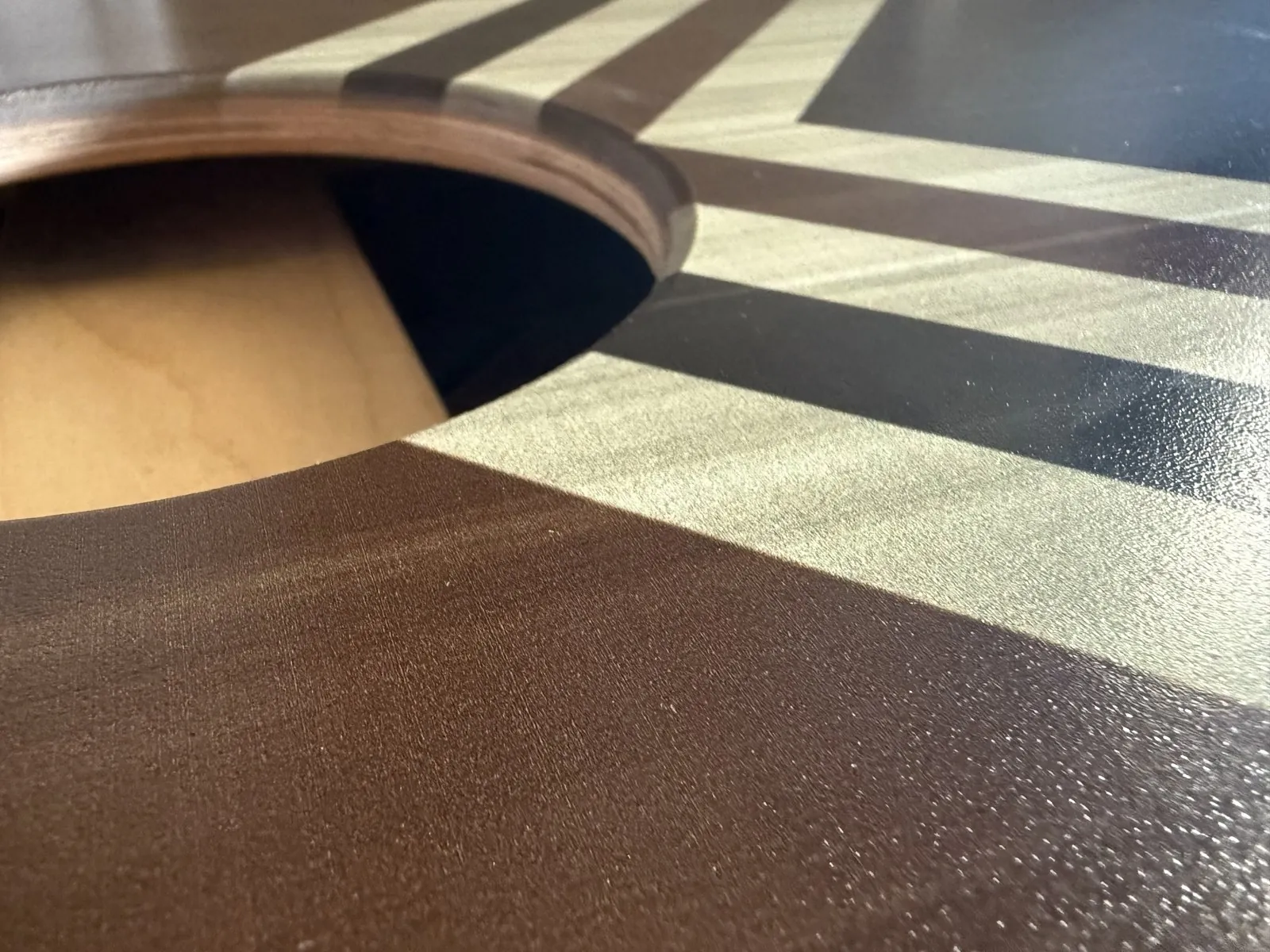 Close-up of a printed board surface showing wood texture through the ink, the plywood laminations at the cut edge of the hole, and clear coat sheen