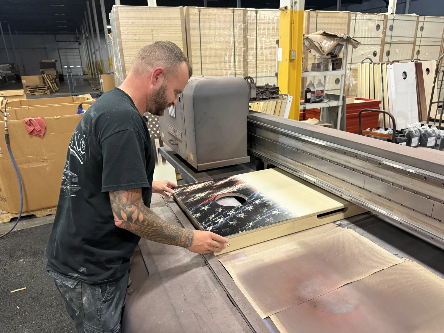Rob loading a printed cornhole board onto the flatbed UV printer at the North Kansas City warehouse